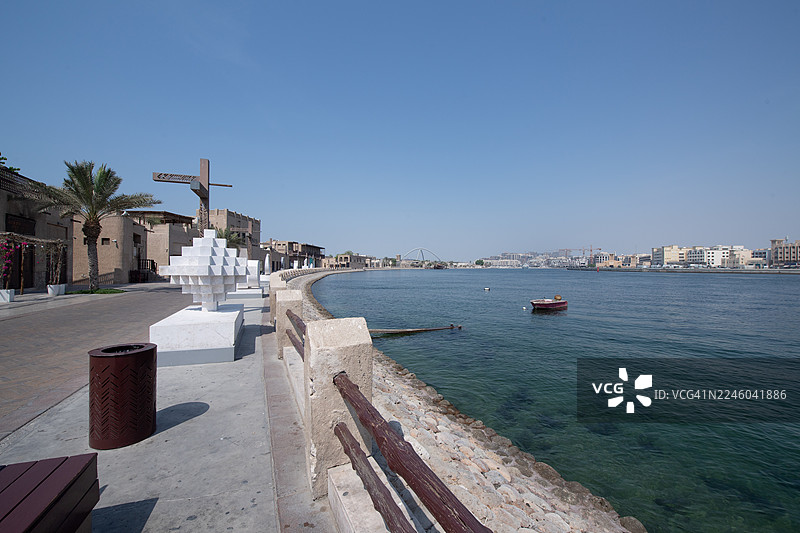 迪拜，阿拉伯联合酋长国，布尔迪拜，晴朗蓝天下的宁静海景，传统建筑和一艘小船在水面上图片素材