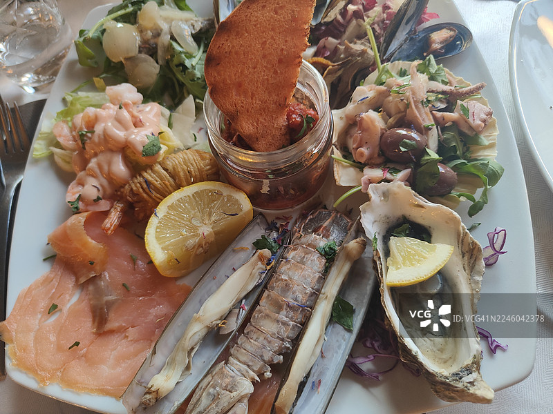白色餐桌上丰盛的海鲜拼盘，俯视角度，包含各种新鲜海鲜、柠檬和面包图片素材