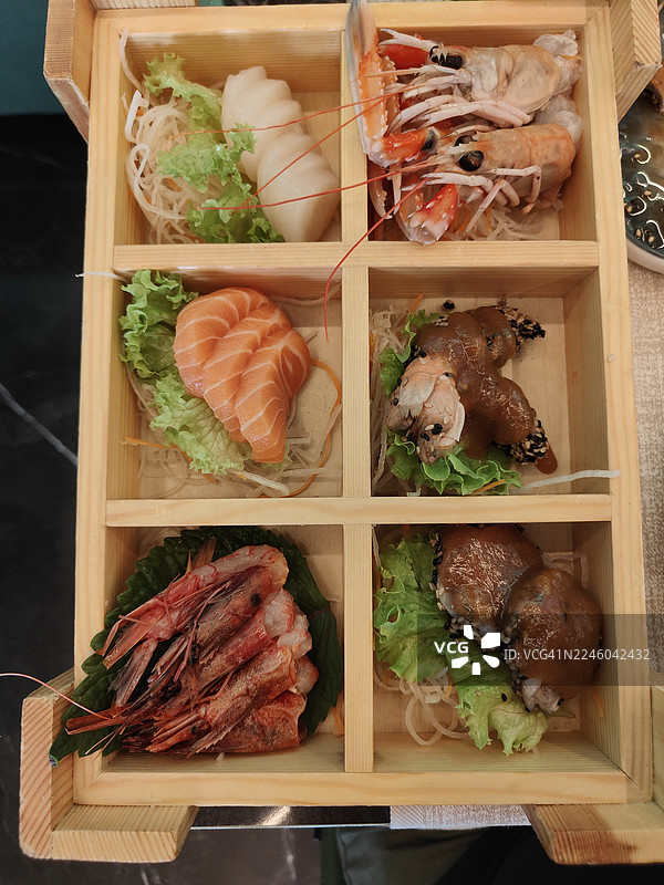 日式便当盒中各种海鲜和生鱼片的俯视特写，放在桌子上图片素材