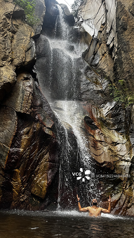 男人在岩石景观中享受天然瀑布的清爽之水图片素材