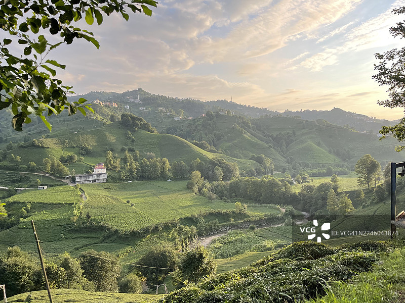 夕阳下，苍翠的农田在起伏的山丘上延伸，远处坐落着村庄，位于土耳其。图片素材