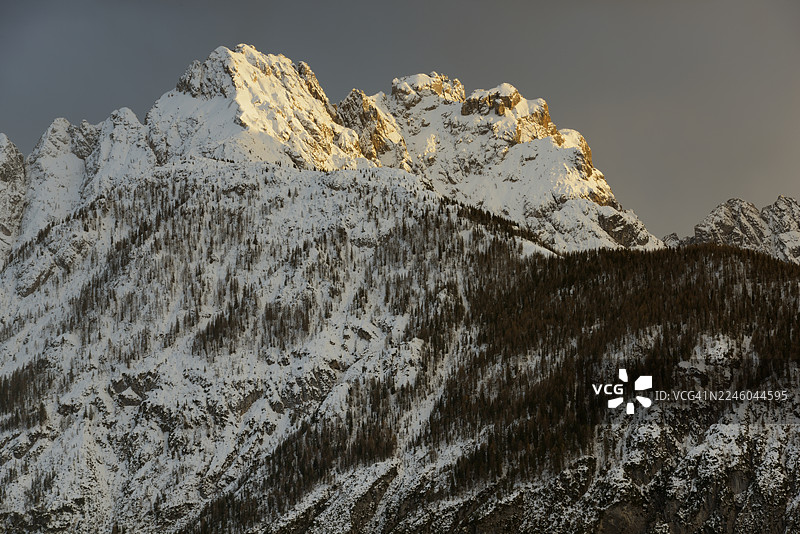壮丽的雪山之巅沐浴在金色阳光下，映衬着戏剧性的天空，意大利科梅利科苏佩里奥雷图片素材