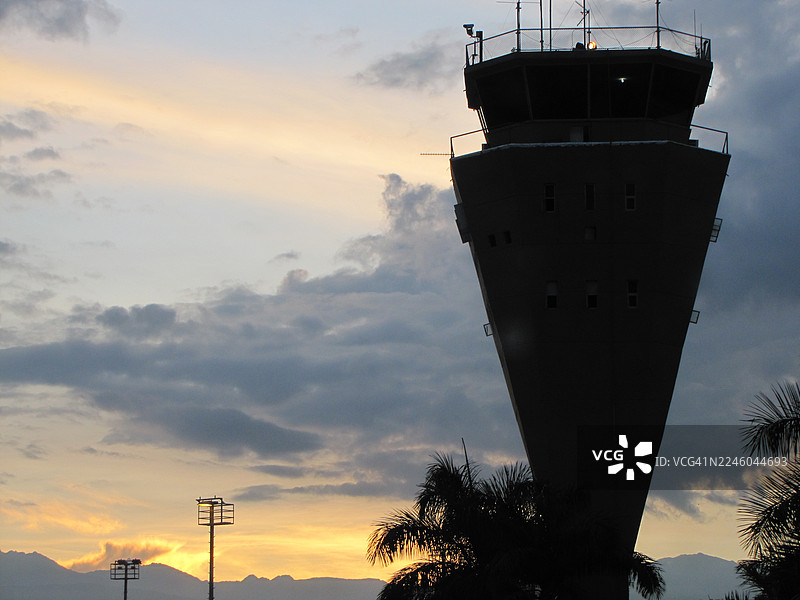 低角度拍摄的机场控制塔，在有云彩和棕榈树的戏剧性日落天空映衬下形成剪影，哥伦比亚帕尔米拉图片素材