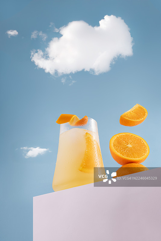 冰镇橙汁配新鲜橙子和冰块，背景是蓝天白云，象征着夏日与清爽图片素材