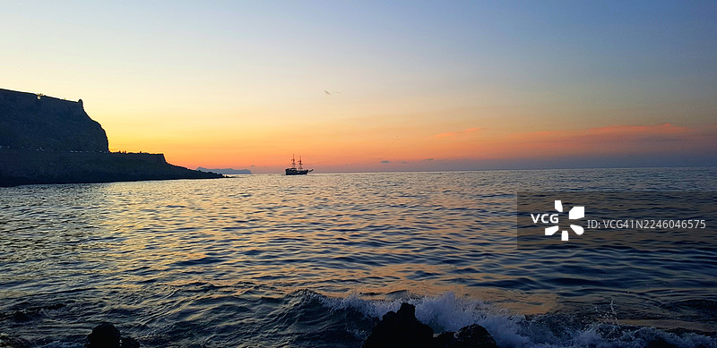 夕阳下的宁静大海与晴朗天空的风景，远处有船只和崎岖的海岸线，希腊雷西姆农。图片素材