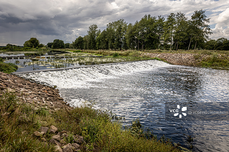 荷兰阿森河畔，风景如画的河流，飞流直下的瀑布，绿意盎然的河岸，以及戏剧性的多云天空。图片素材