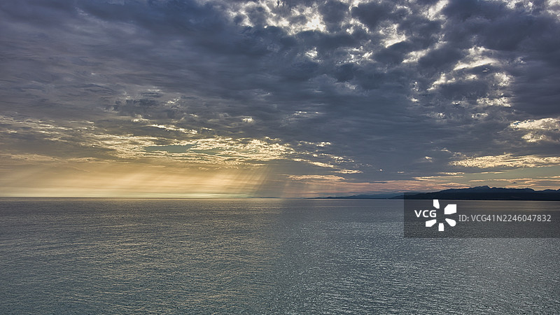 西班牙萨洛卡尔萨卢海边壮丽的日落，阳光穿透乌云，远方可见山峦图片素材