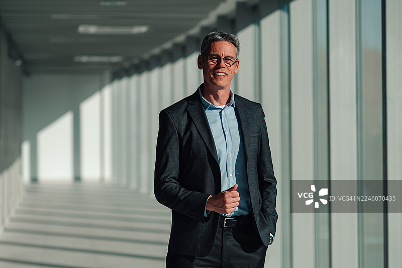 成熟的商务男士自信地笑着走在现代化的办公楼走廊里图片素材