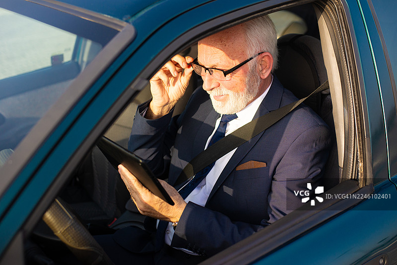 年长的商务男士坐在车内，面带微笑地使用平板电脑图片素材