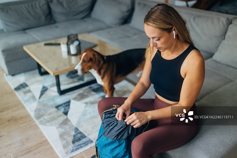 一位活跃的女性坐在时尚的家中，正在收紧背包的抽绳。这张图片强调了准备、旅行就绪和冒险规划。图片素材