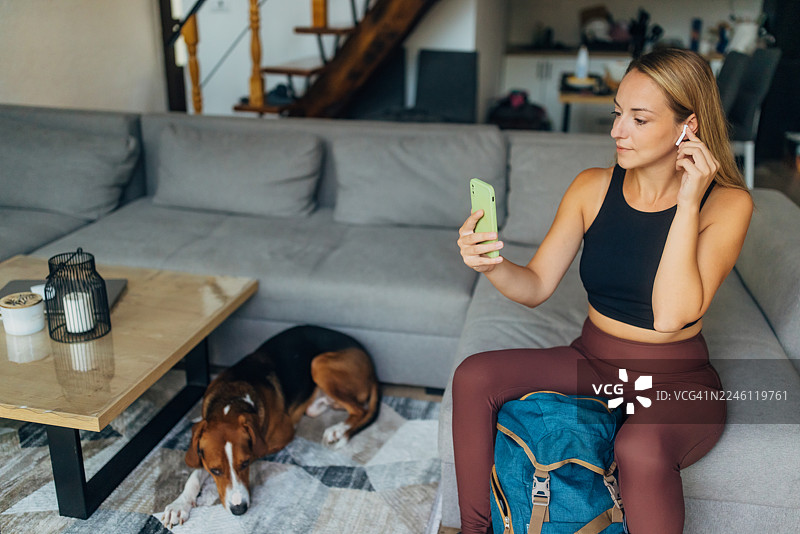 一只猎犬躺在旁边，一位女士坐在沙发上戴上耳机，准备开始户外徒步探险。图片素材