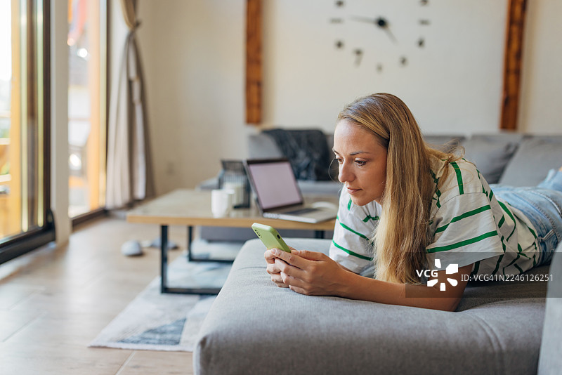 一位女士正在度假，躺在沙发上，使用手机，享受宁静祥和的时光图片素材
