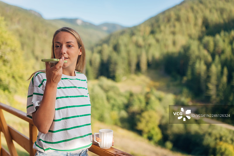 女子在山景阳台上用智能手机发送语音消息图片素材