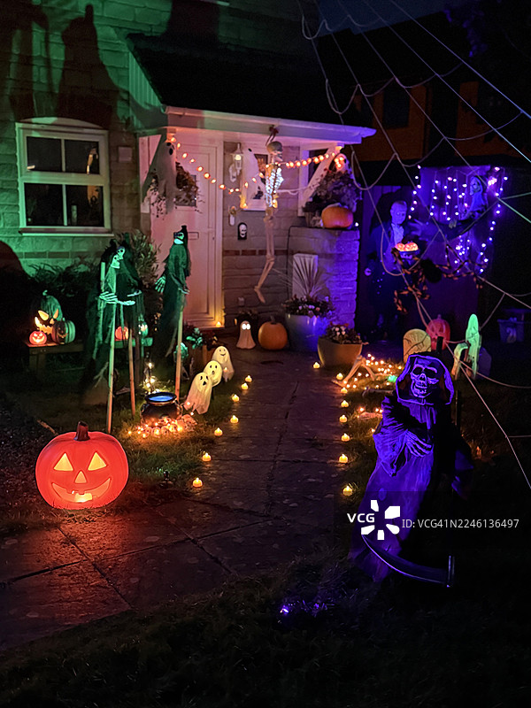 充满活力的前院万圣节装饰，有恐怖的骷髅、南瓜、鬼魂、紫色和绿色串灯、怪物、坟墓和墓碑。图片素材