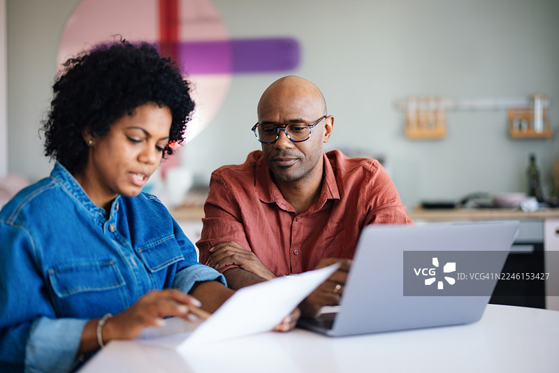 一对情侣在家中一起查看家庭账单和预算，旁边有笔记本电脑和文件。图片素材