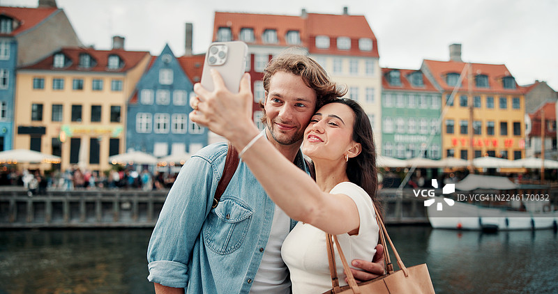 快乐情侣在城市度假，在河边拍摄旅行自拍，用于摄影或户外留念。男女两人微笑或拥抱，定格假期或蜜月湖畔的美好瞬间。图片素材