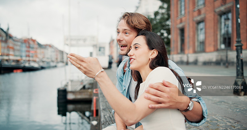快乐的情侣在城市度假、周末出游或户外度假，拥抱旅行和观光。男女在湖边或河边微笑指向，共度蜜月旅行、旅游或城镇之旅。图片素材