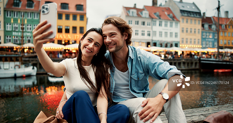 快乐的情侣在湖边或河边拥抱自拍，记录下城市旅行中的美好瞬间，为照片、回忆、假期、约会或蜜月留下纪念。图片素材