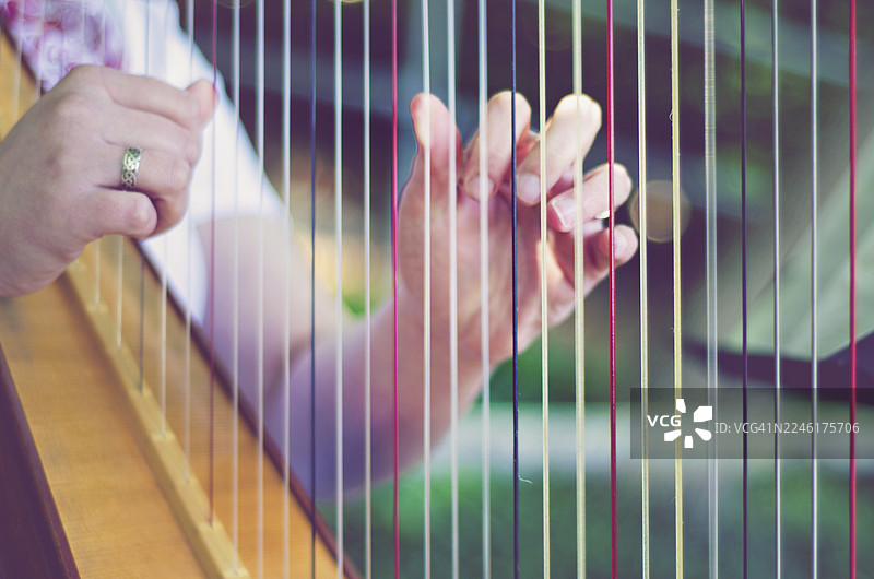 一位音乐家的手优雅地拨动着竖琴的琴弦，特写镜头和浅景深聚焦于鲜艳的红白琴弦。这张图片传达了演奏这种古典乐器所蕴含的艺术性和细腻的触感。图片素材