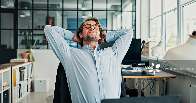 男人在办公室里完成任务或截止日期后的休息、放松和满足。快乐的员工在工作场所将手放在头后面伸展，享受宁静、安逸和健康。图片素材