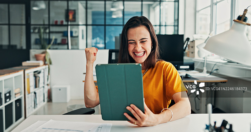 快乐的女性，在办公室里，举着平板电脑或握紧拳头，庆祝好消息或晋升。兴奋的女性，面带微笑，使用科技，庆祝在线评论或奖金。图片素材