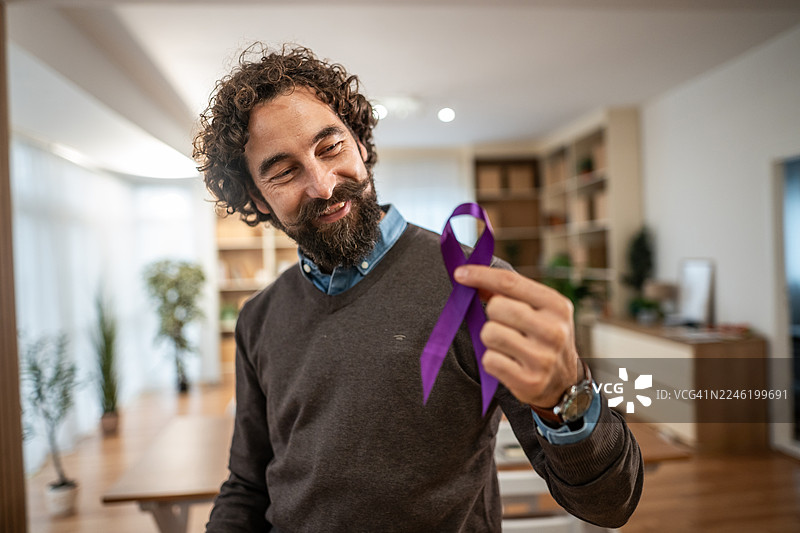 男子在室内手持紫色丝带，象征意识与支持图片素材