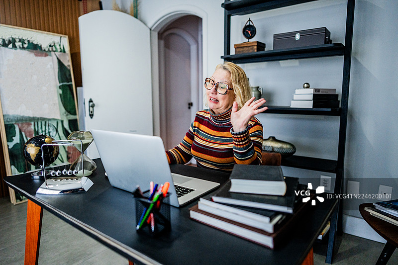一位年长的女性在办公室使用笔记本电脑进行视频通话并喝咖啡图片素材
