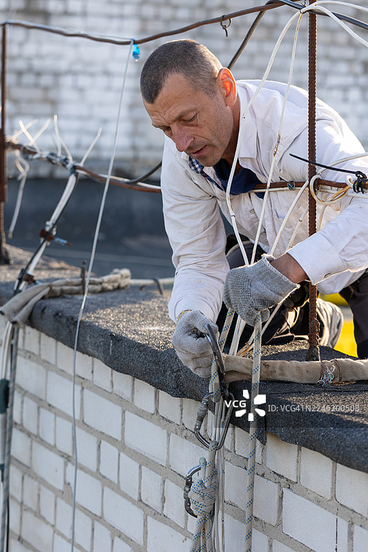 建筑工人正在居民楼屋顶边缘固定安全绳准备下降。图片素材