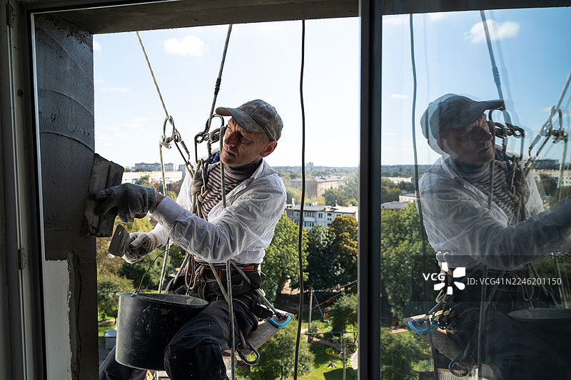 一名建筑工人正在居民楼九层高处粉刷窗户斜坡。图片素材