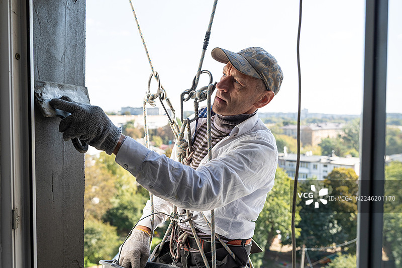 一名建筑工人在居民楼九楼的高度抹窗户斜坡。图片素材