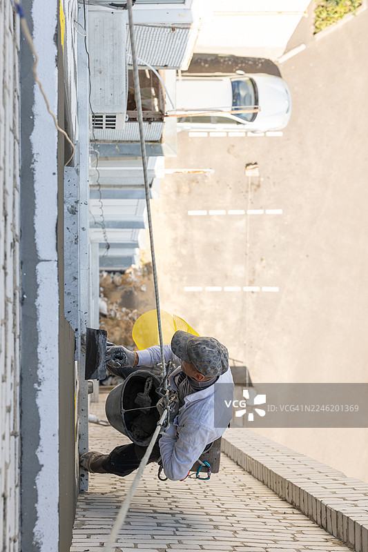 建筑工人正在用粘合剂覆盖钢筋网。他正在为九楼的建筑外墙进行保温。图片素材