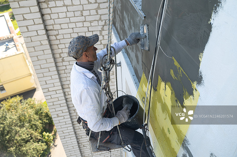 建筑工人正在用粘合剂覆盖钢筋网。他正在为九楼的建筑物进行外墙保温施工。图片素材