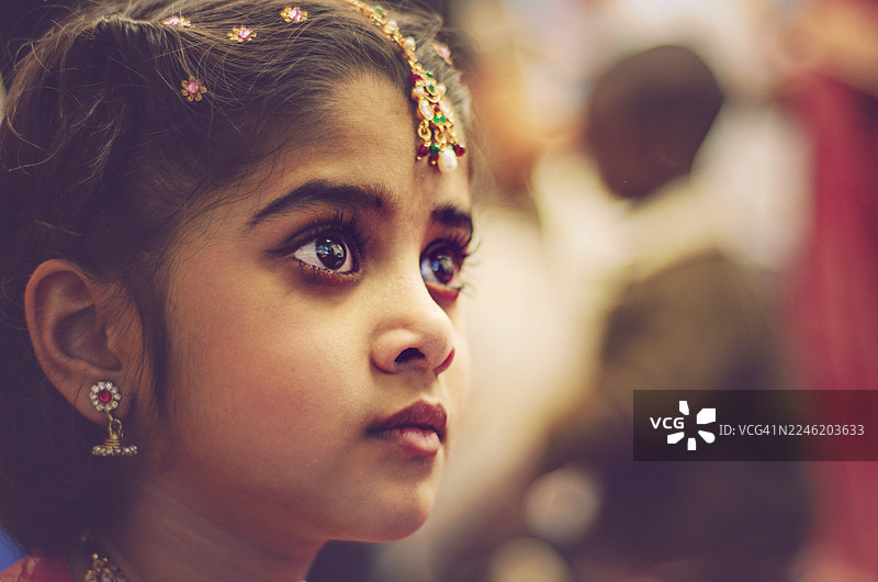 一位年轻女孩佩戴着印度传统珠宝，包括额饰和发簪，用富有表现力的眼睛看着镜头。她的脸妆以眼线和红唇为特色，突显了文化之美和节日盛装。图片素材