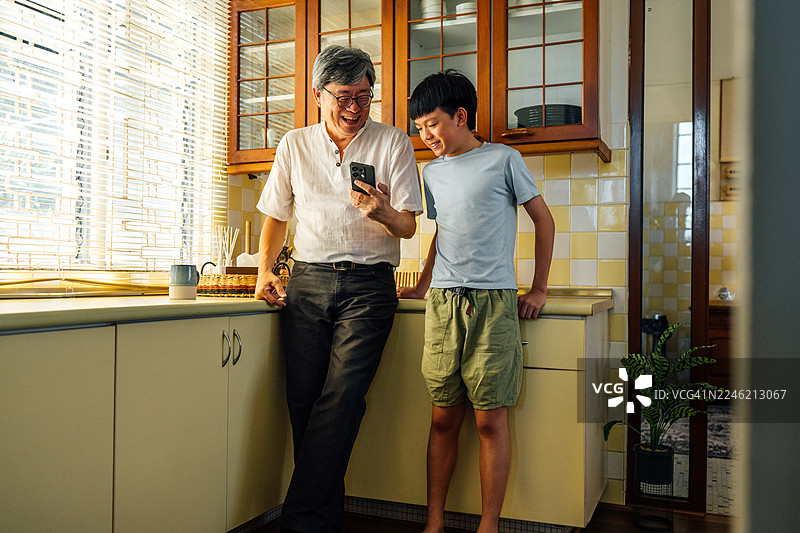 一位精通科技的亚裔爷爷在使用智能手机，同时和他的孙子享受欢乐时光图片素材