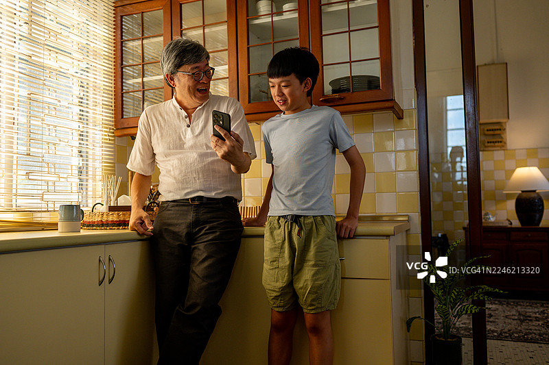 亚裔孙子与现代祖父一起玩智能手机，其乐融融。图片素材