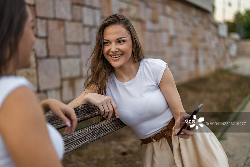 一位美丽的自由职业者坐在河边长椅上，用手机讨论工作并查看她视频的分享。图片素材