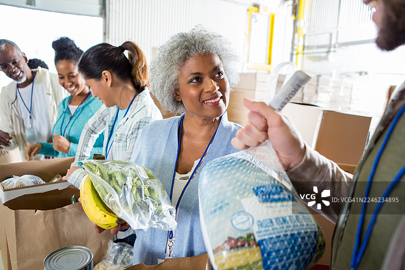 一群面带笑容的多元化志愿者正在打包食品捐赠，以用于社区外展活动。图片素材