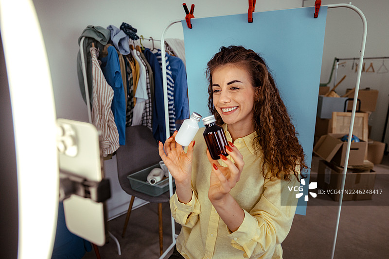 女子在家中使用智能手机和环形灯拍摄美妆产品视频图片素材