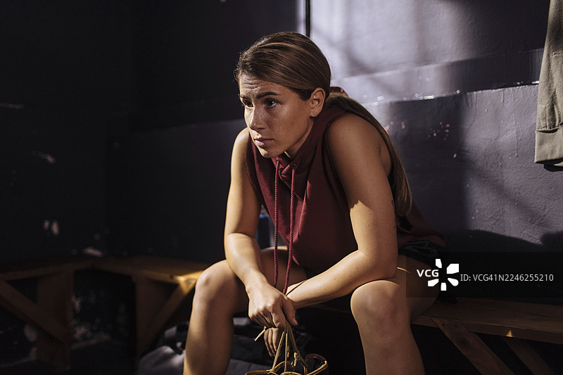 年轻女子坐在昏暗房间的长椅上，情绪内省，身穿红色无袖连帽衫图片素材