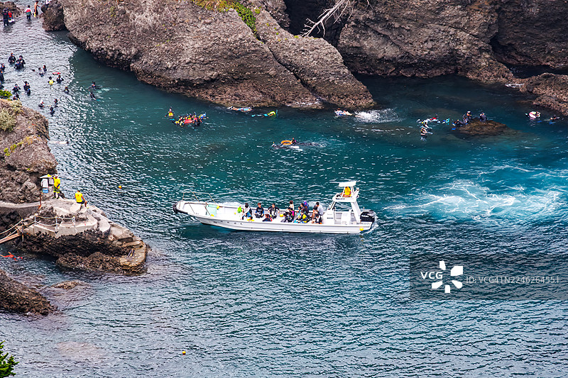 从海角天文台俯瞰的日御崎海滩绝美的蔚蓝大海。可以看到御藏岛等无人岛、小岛以及当地的岩石海岸。潜水员和浮潜者乘着渔船在海上渡轮上。图片素材
