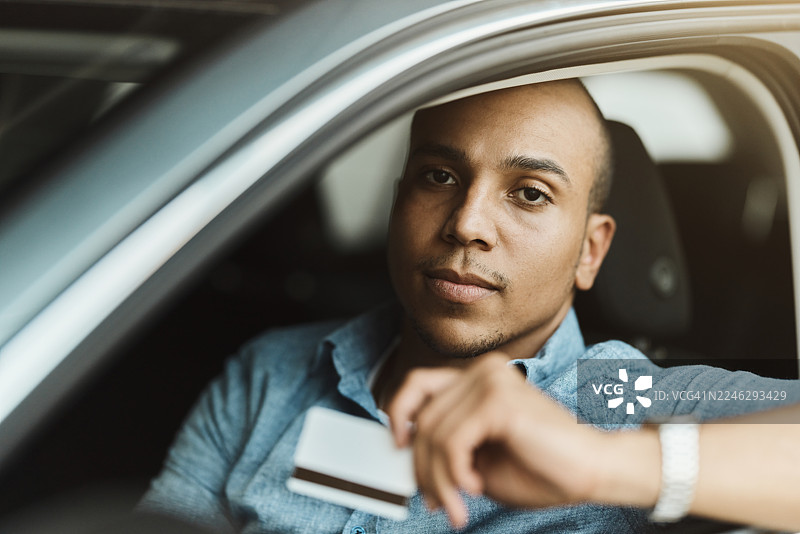 年轻的黑人男子一边开车一边使用信用卡。图片素材