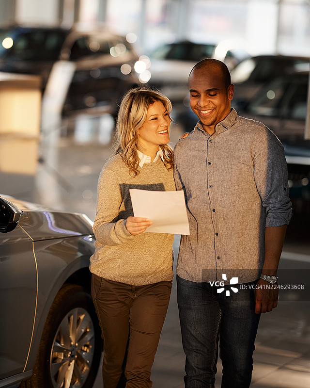 一对快乐的多元化情侣在汽车展厅的车内阅读文件。图片素材