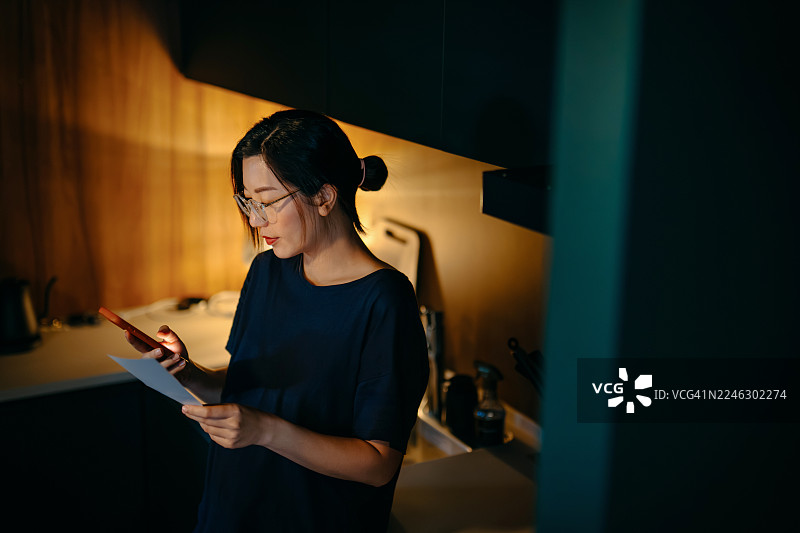 年轻亚洲女性在家中厨房的柜台上计算财务账单和收据，管理个人银行和财务。在家中规划预算和计算开支。家庭预算。家庭财务概念。图片素材