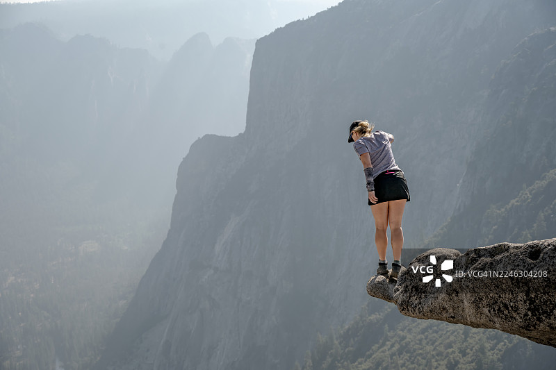 一位年轻女子站在美国加利福尼亚州优胜美地国家公园风景如画的陡峭悬崖上图片素材