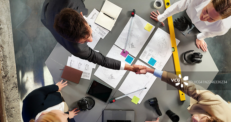 建筑、握手和会议中的人们，用于建筑设计、平面图或翻新。握手、承包商和工人进行协议、蓝图或改造项目规划。图片素材