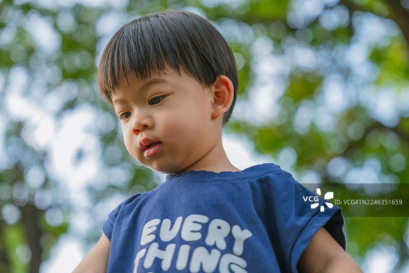 小小的亚洲孩童，学步的男孩，在阳光明媚、树影婆娑的自然花园或公园里，充满乐趣地奔跑、玩耍、探索和学习，享受着大自然的清新与活力。图片素材