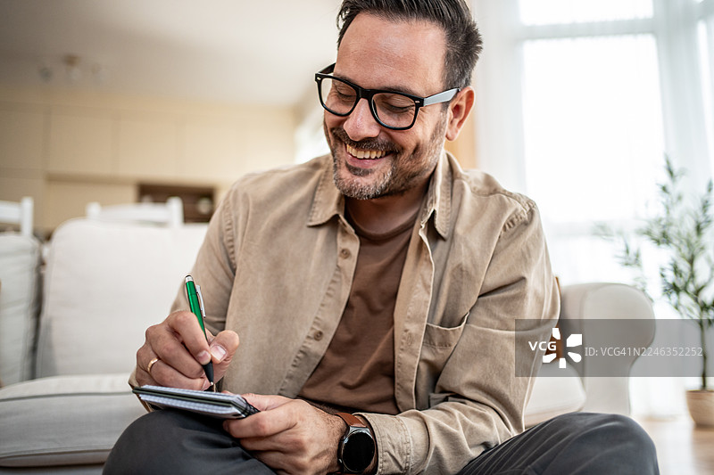 快乐的男人在家里的笔记本上写笔记图片素材