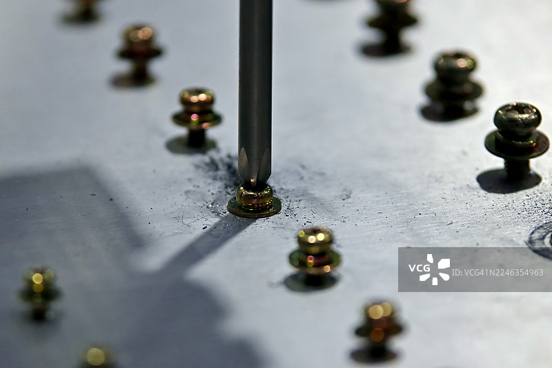 精密紧固。特写镜头展示一把十字螺丝刀正在金属表面上固定一颗金色螺丝图片素材