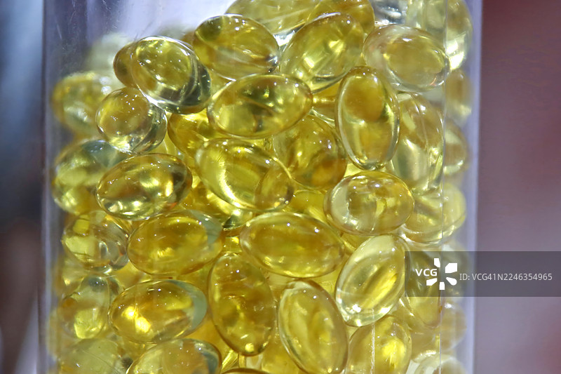 大量半透明椭圆形软胶囊的特写，很可能是欧米茄3或维生素D，装在透明塑料瓶中图片素材