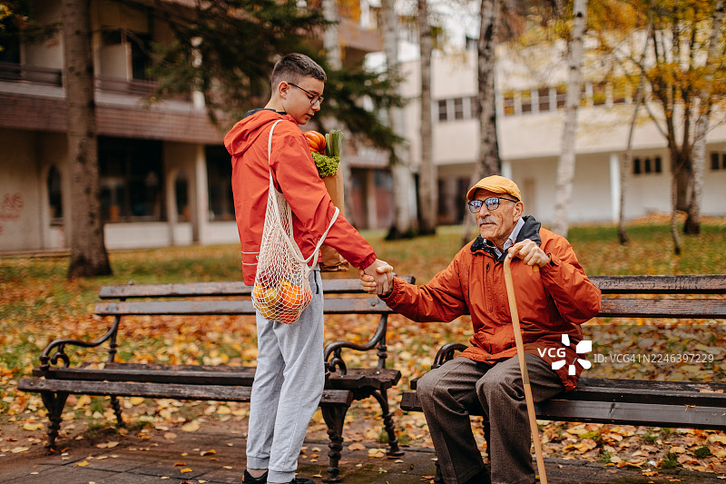 青少年男孩帮爷爷提着纸袋子里的杂货，并搀扶他站起来图片素材